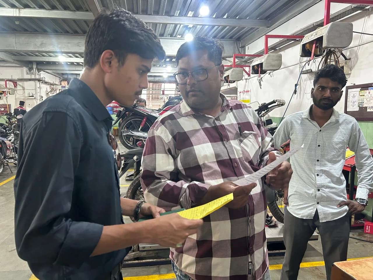 Reviewing printed service documents with mechanics inside a two-wheeler repair workshop