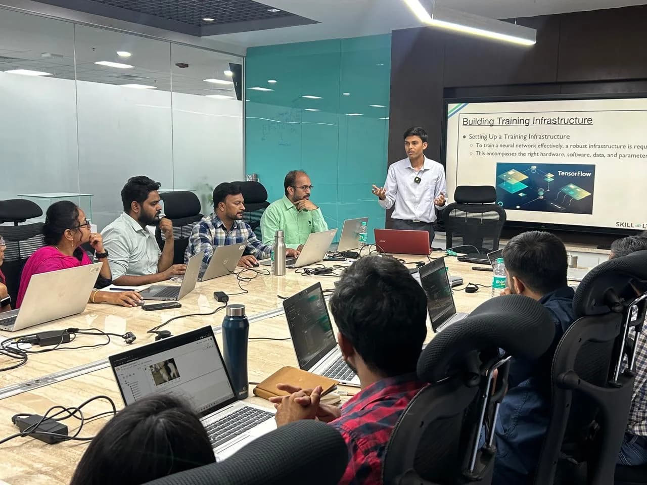 Presenting a slide on training infrastructure and TensorFlow to professionals seated with laptops