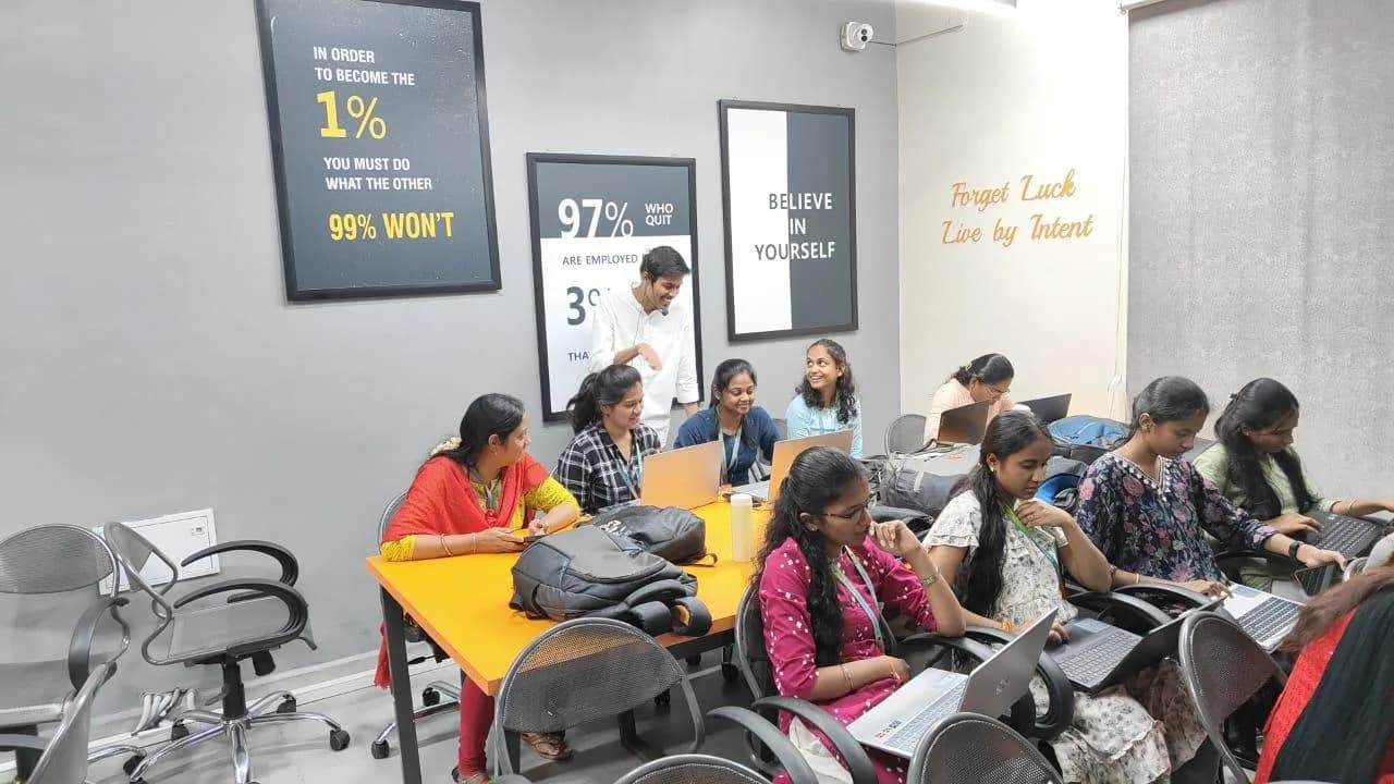 Instructor talking with students working at laptops in a training room