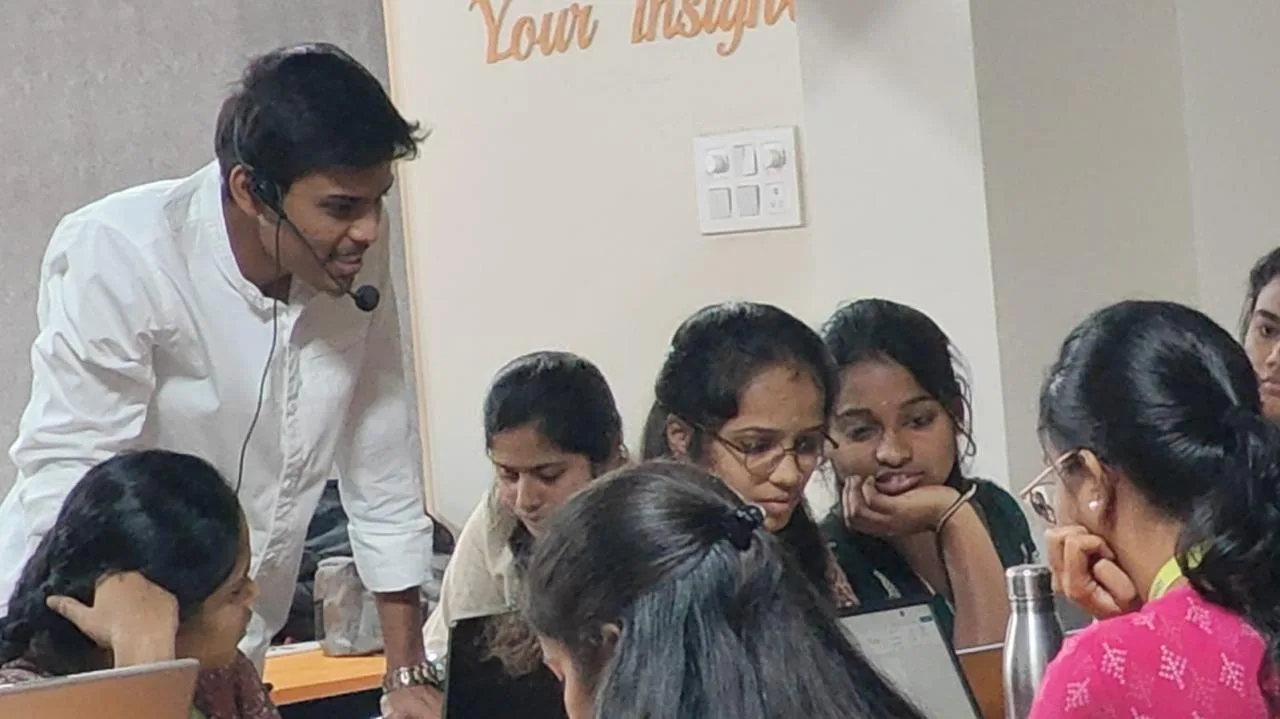 Instructor leaning in to look at a student laptop screen surrounded by attendees